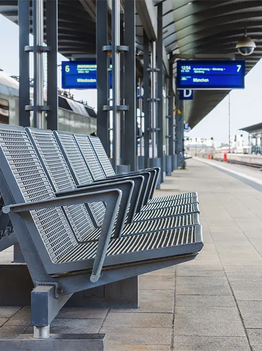 Sitzgruppe zum Warten auf einem Bahnsteig mit digitaler Zuganzeige im Hintergrund (themenunterstützendes Bild)