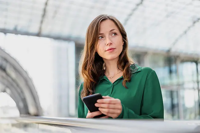 Smart sustainability: Woman with smartphone in hand waiting on the platform (topic-supporting image)