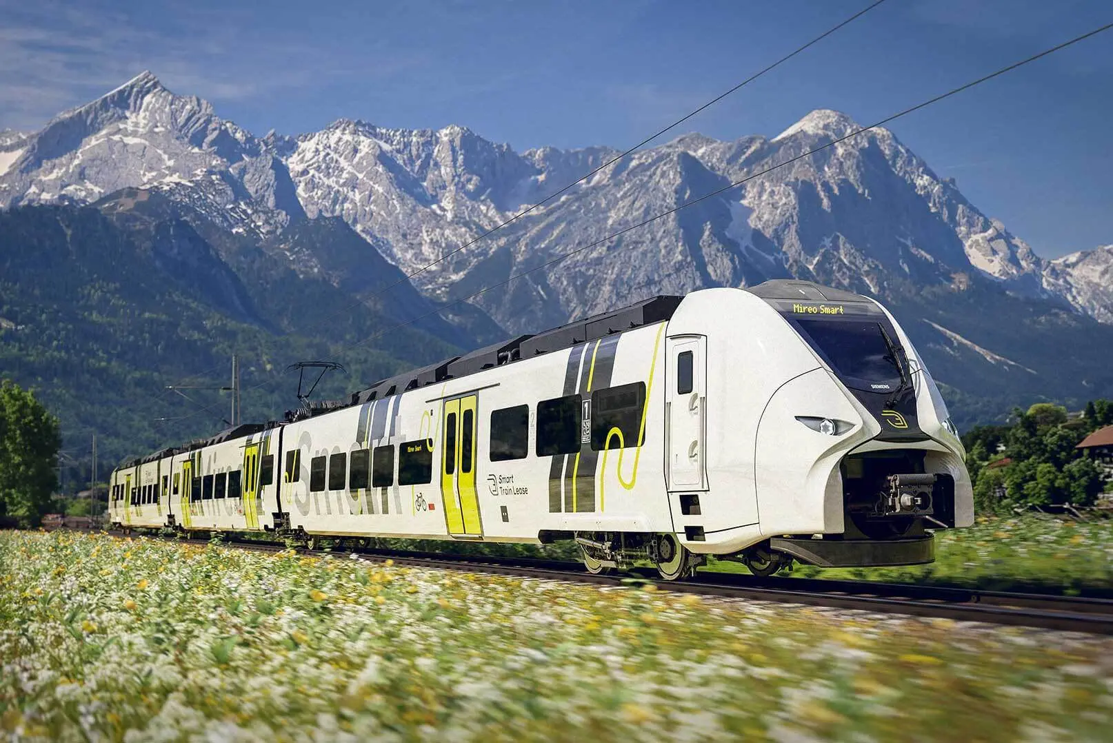 A driving Siemens Mireo Smart rental train photographed frontal/sideways in front of a Bavarian mountain panorama, sunny weather
