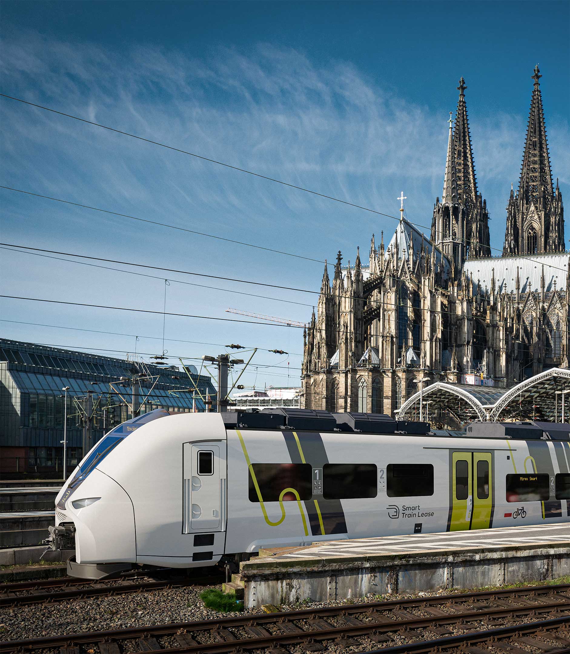 Ein am Bahnhof stehender Siemens Mireo Smart Miet-Zug, fotografiert seitlich von vorne mit Kölner Dom im Hintergrund